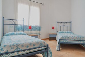 A room with two beds, each with a patterned bedspread and a red lamp on a bedside table.