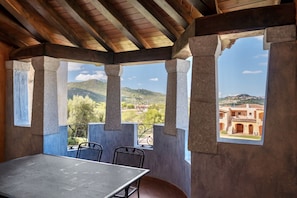 A covered outdoor seating area with a table and chairs, large windows, and a view of a distant building.