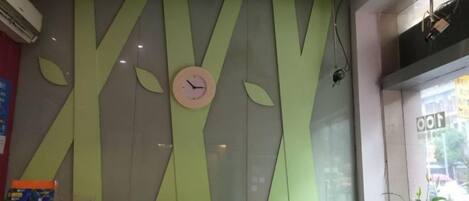 A reception area with a clock, a plant, and a QR code stand.
