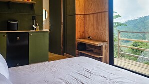 Een slaapkamer met een groot bed, houten plafond, uitzicht op de omgeving en een kleine kitchenette.