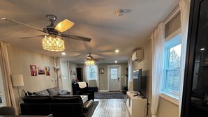 A modern living room with a sofa, a dining table with chairs, a ceiling fan, and a chandelier. - Clementsvale Oasis: Rest, Recharge, and Explore. (Clementsvale)
