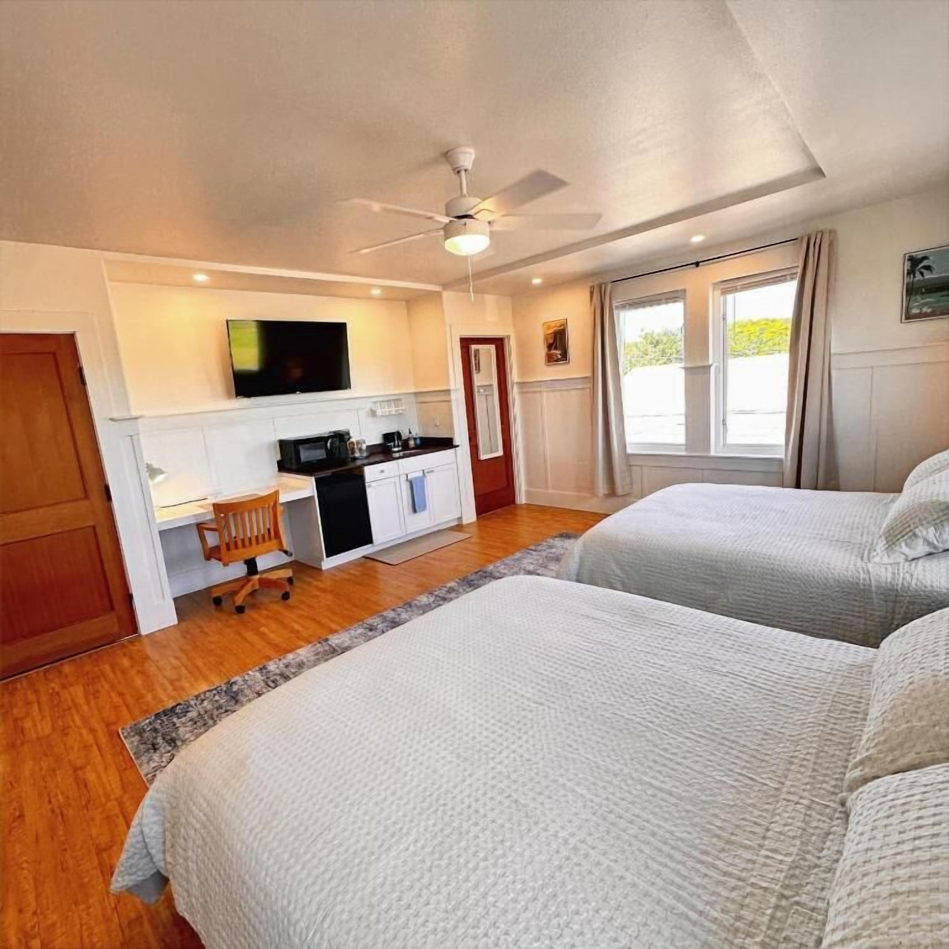 A bedroom with two beds, a desk, a chair, a TV, and a window with curtains.