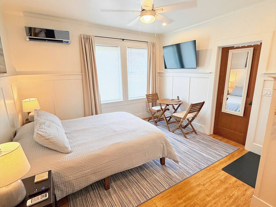 A hotel room with a bed, a desk with a lamp, a chair, a television, and a ceiling fan.