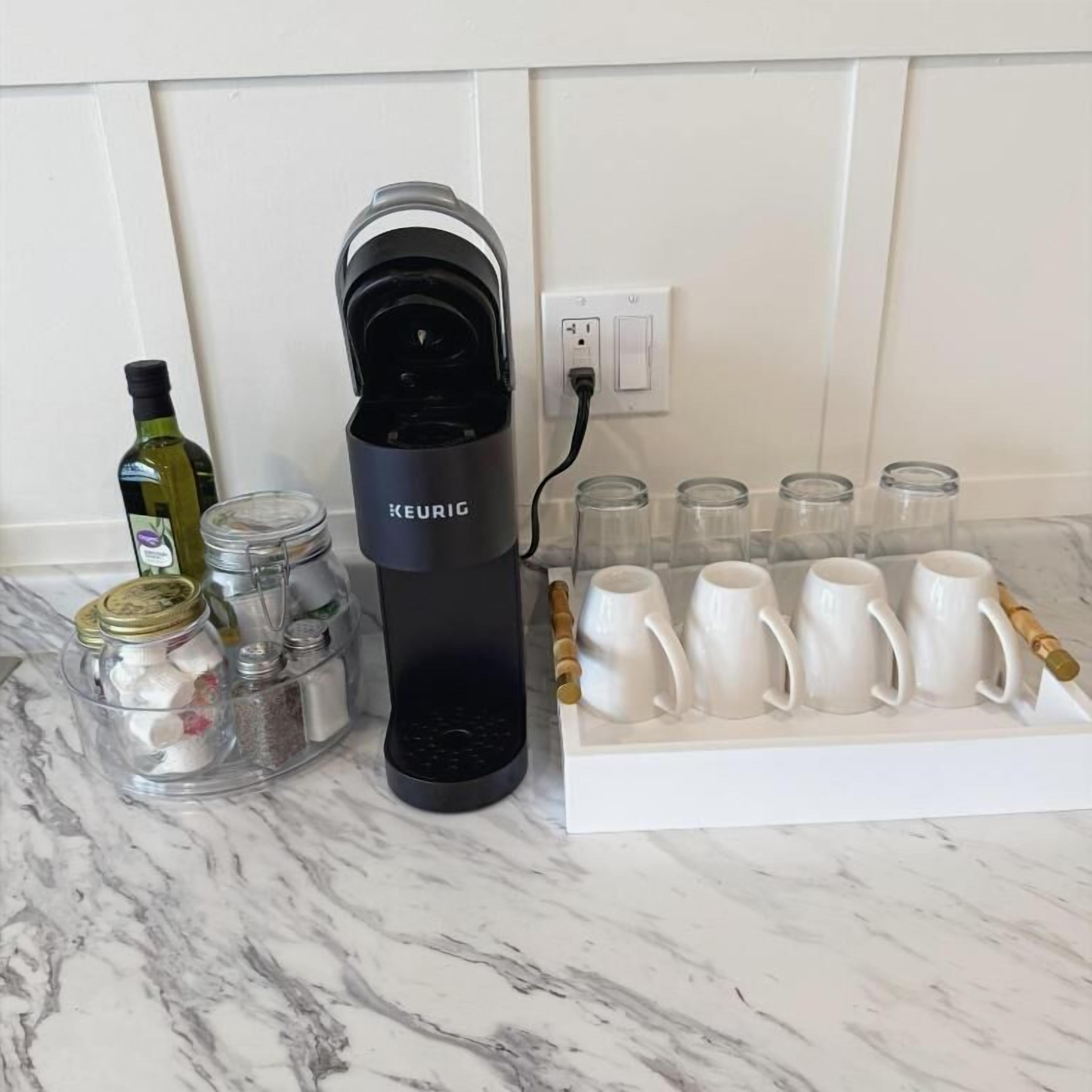 Une cuisine équipée d’une machine à café Keurig, d’une bouteille d’huile d’olive et d’un ensemble de tasses blanches posées sur un plan de travail en marbre.