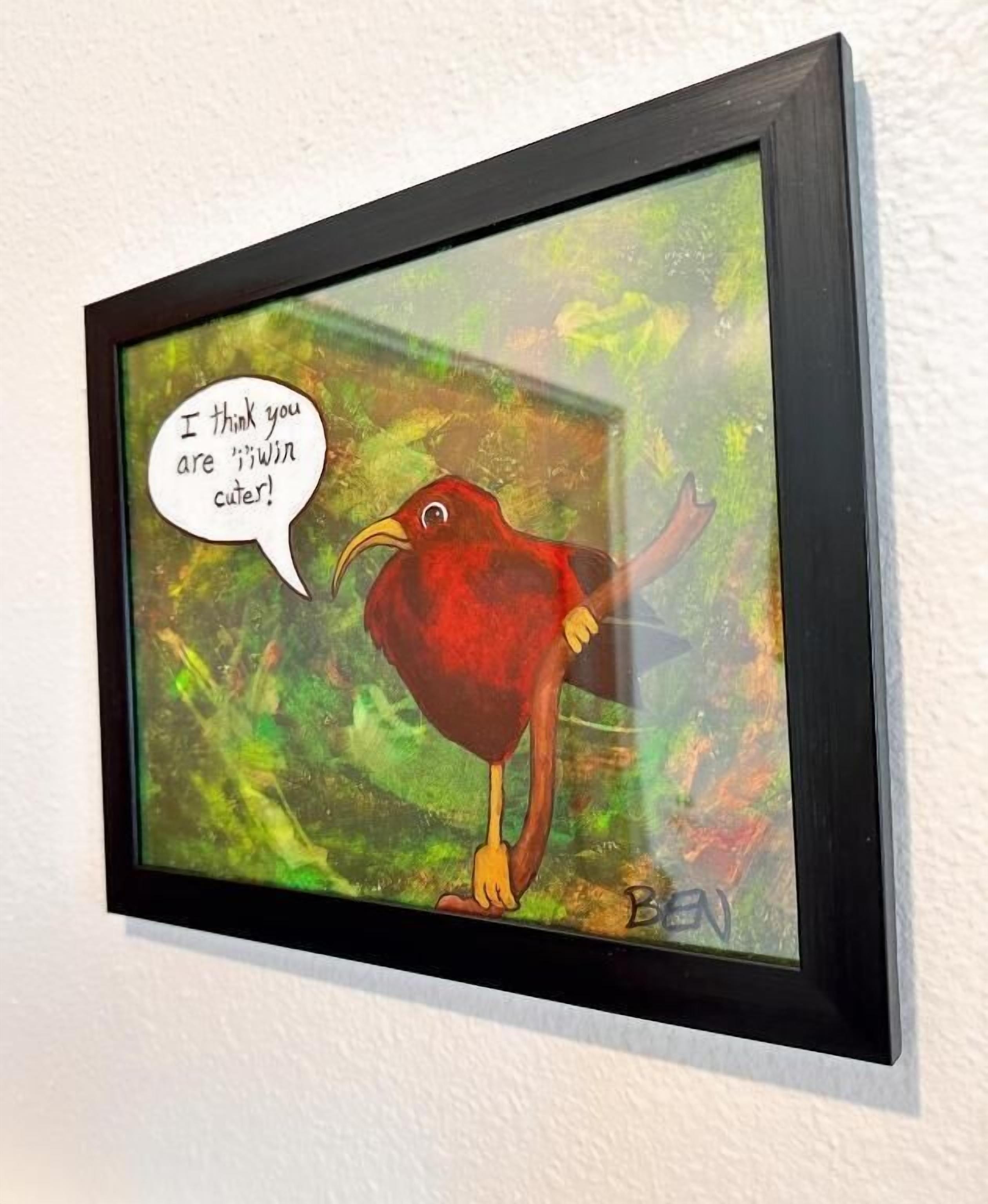 Une œuvre d’art encadrée représentant un oiseau rouge, avec une bulle de dialogue indiquant : « Je trouve que tu es beaucoup plus mignon(ne) ! », est accrochée à un mur blanc.