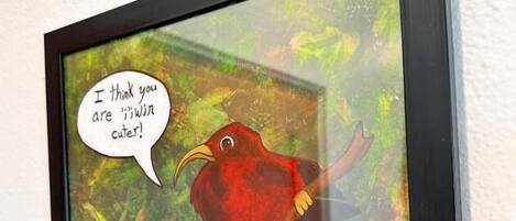 Une œuvre d’art encadrée représentant un oiseau rouge, avec une bulle de dialogue indiquant : « Je trouve que tu es beaucoup plus mignon(ne) ! », est accrochée à un mur blanc.