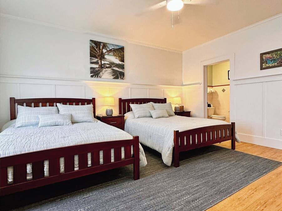 A bedroom with two wooden beds, a ceiling fan, and a gray rug.