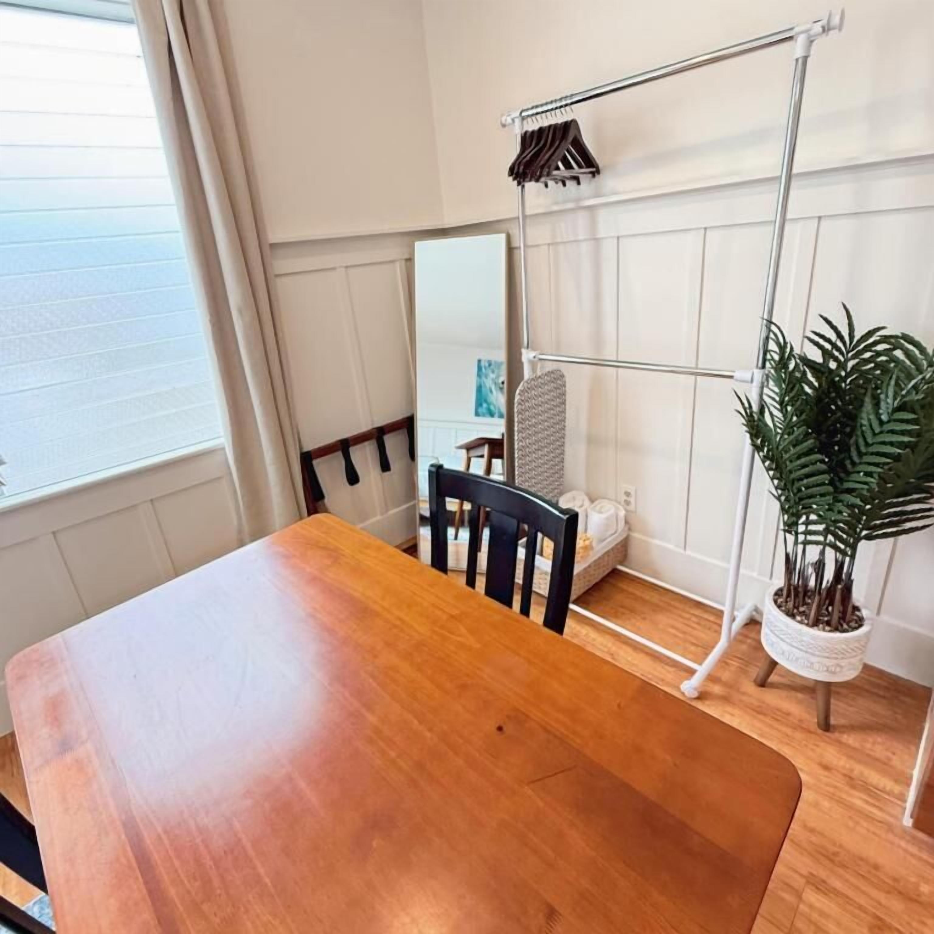 A wooden dining table with chairs, a metal towel rack, a potted plant, and a large mirror on the wall.