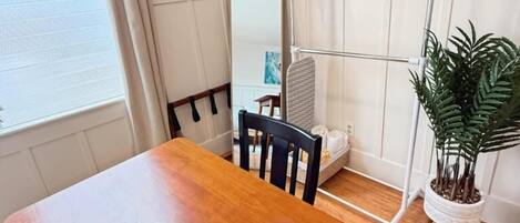 A wooden dining table with chairs, a metal towel rack, a potted plant, and a large mirror on the wall.