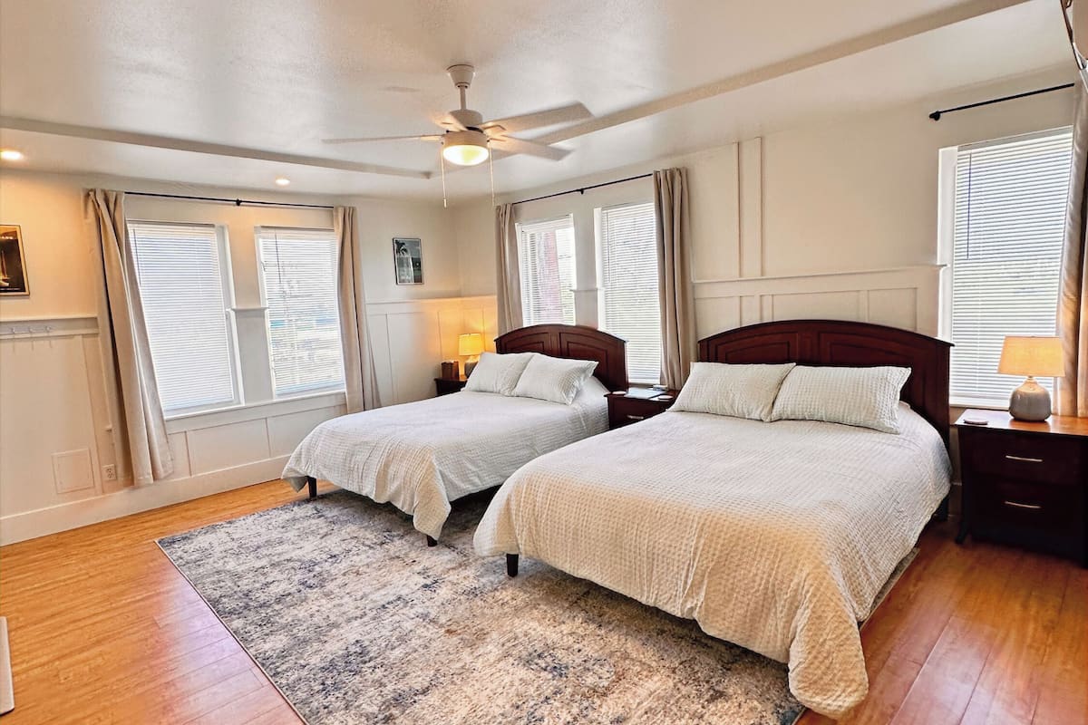 A bedroom with two beds, a ceiling fan, and a large window with blinds.