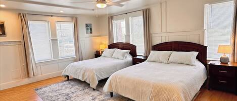 A bedroom with two beds, a ceiling fan, and a large window with blinds.