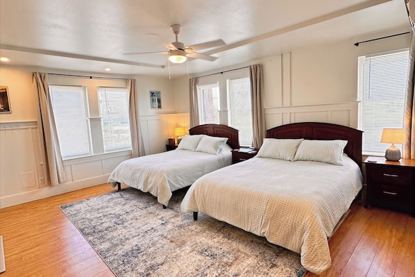 A bedroom with two beds, a ceiling fan, and a large window with blinds. - Hilo Town Inn (Hilo)