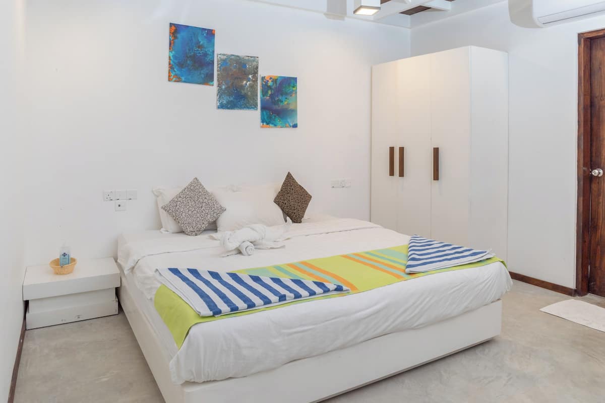 Een moderne slaapkamer met een groot bed, witte muren en abstracte kunst.