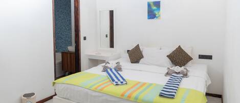 Una habitación de hotel con una cama grande, una mesita de noche, un espejo y un cubo de basura pequeño.