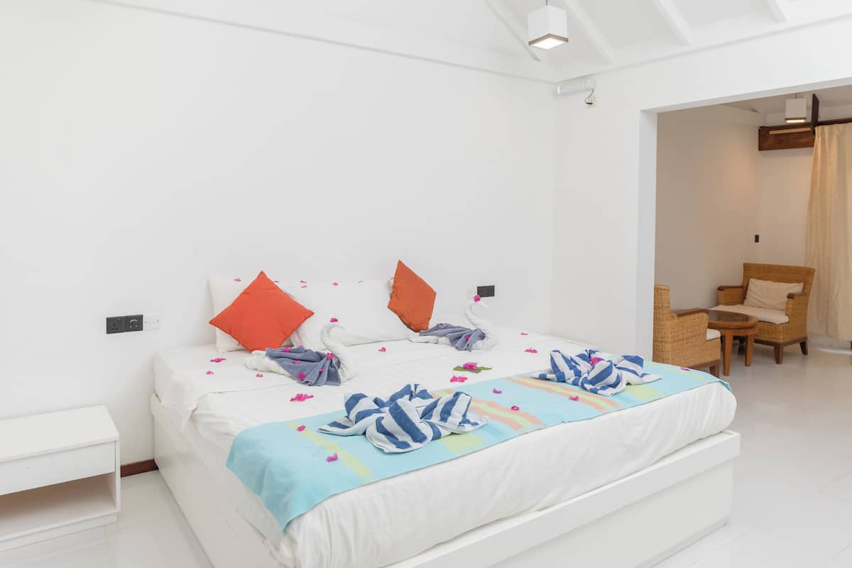 Een moderne hotelkamer met een groot bed, witte muren en een klein zithoekje met een stoel en een tafeltje.