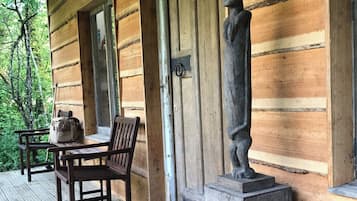 A wooden cabin with a porch, a bench, a table, and a statue.