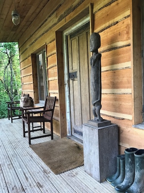 A wooden cabin with a porch, a bench, a table, and a statue.