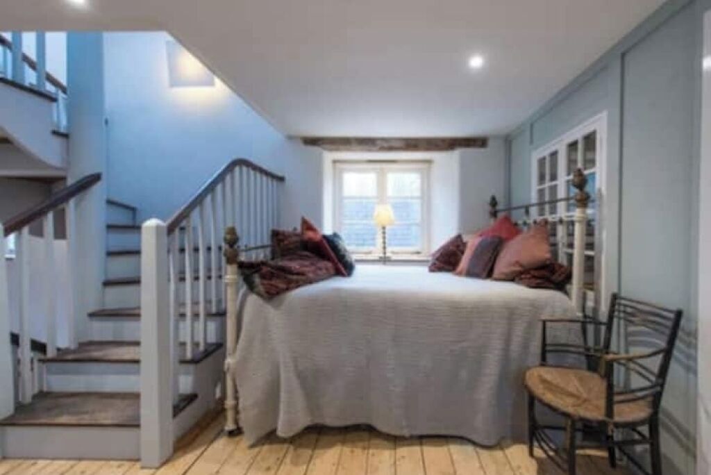 A bedroom with a bed, a chair, a window, and a staircase.