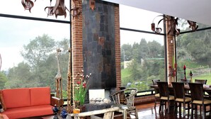 Una habitación amplia con un gran ventanal, chimenea, sofá rojo, sillas de madera y una mesa de comedor.