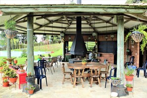 Een terras buiten met een houten tafel en stoelen, omringd door plantenpotten en een bakstenen muur.