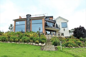 Een modern herenhuis met twee verdiepingen, een balkon, grote ramen en een verzorgde tuin.