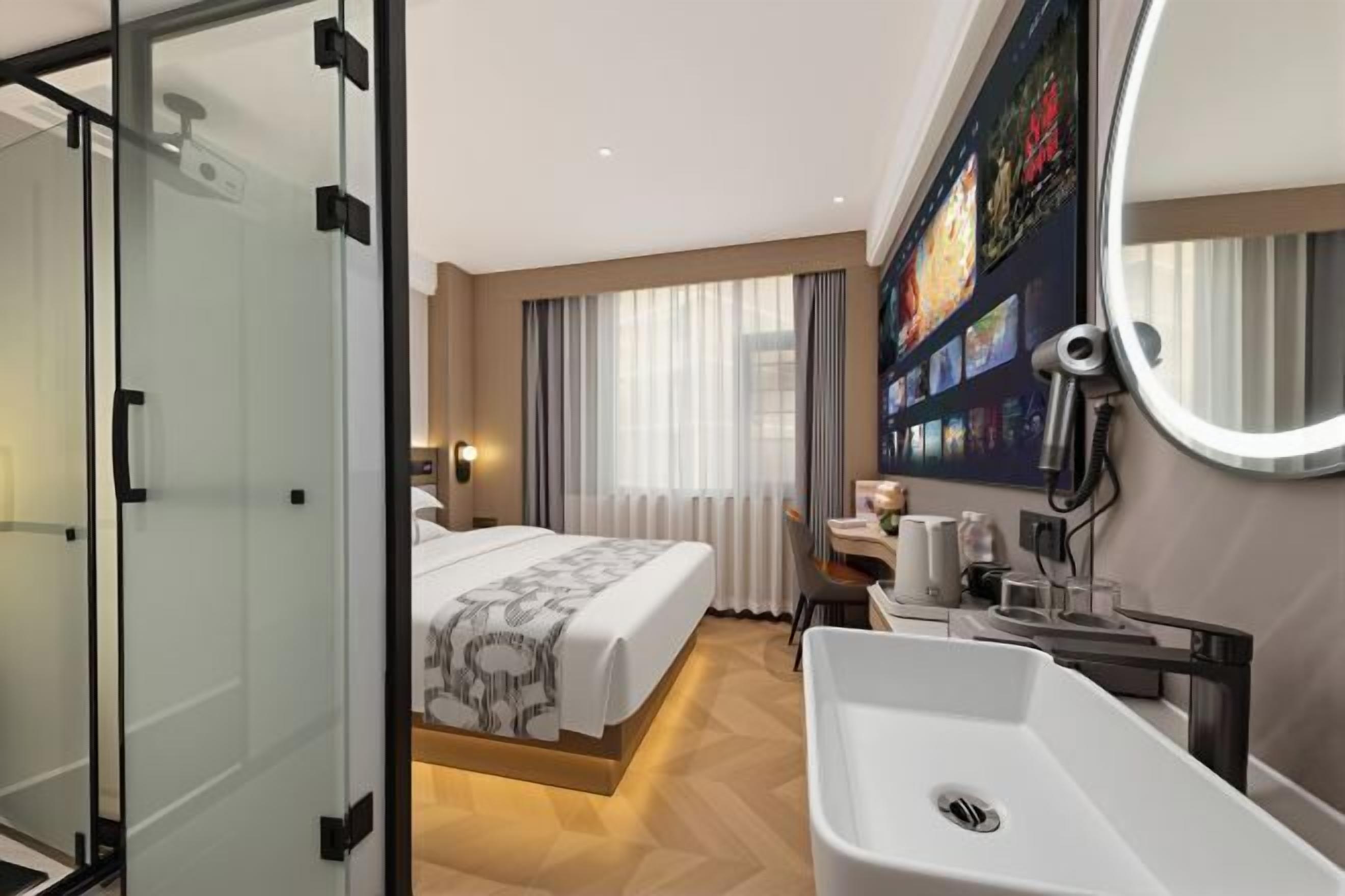 A hotel room with a bed, a bathroom with a sink, a mirror, and a wall-mounted TV.