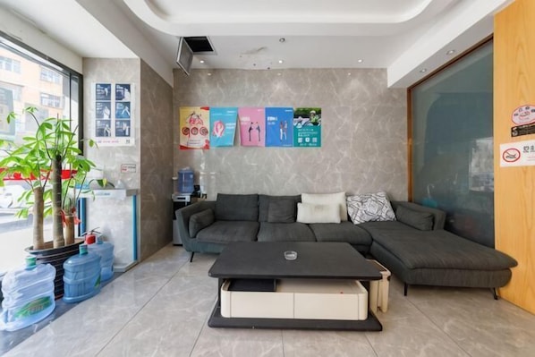 A modern hotel lobby with a sectional sofa, a coffee table, a potted plant, and informational posters on the wall. - Huatian Business Hotel (Shenzhen)