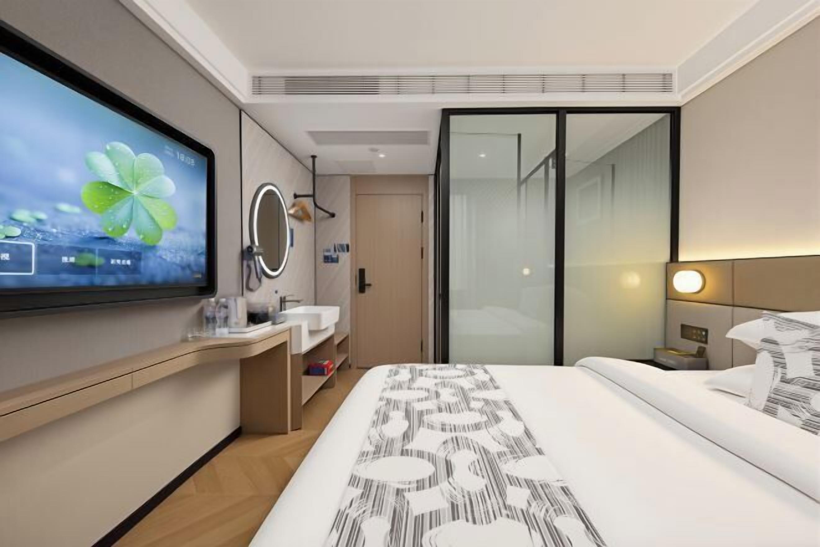 Ein modernes Hotelzimmer mit einem großen Bett, einem Flachbildfernseher, einem Badezimmer mit Spiegel und einem Schiebetürenschrank.