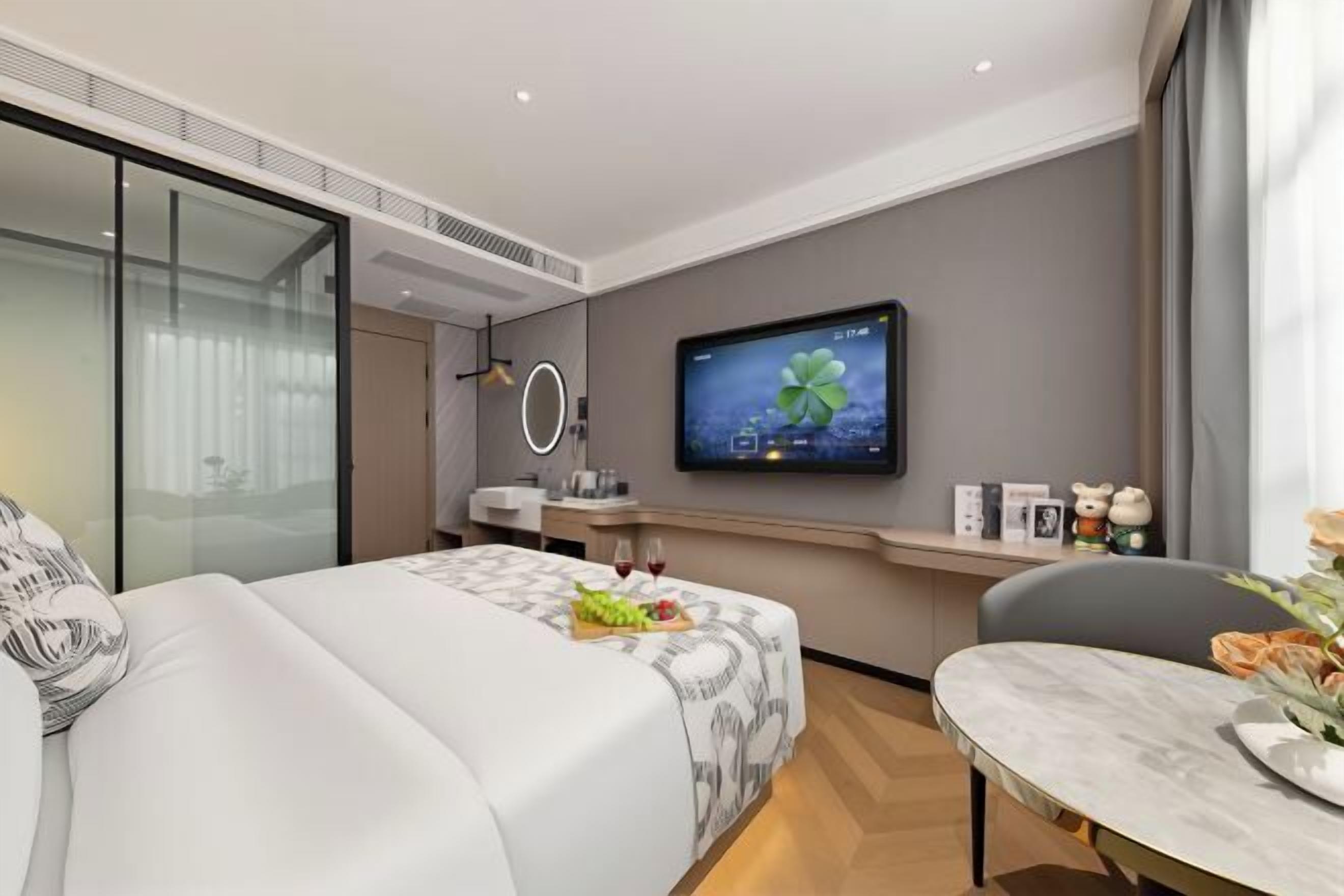 A modern hotel room with a bed, a desk, a television, and a view of the city.
