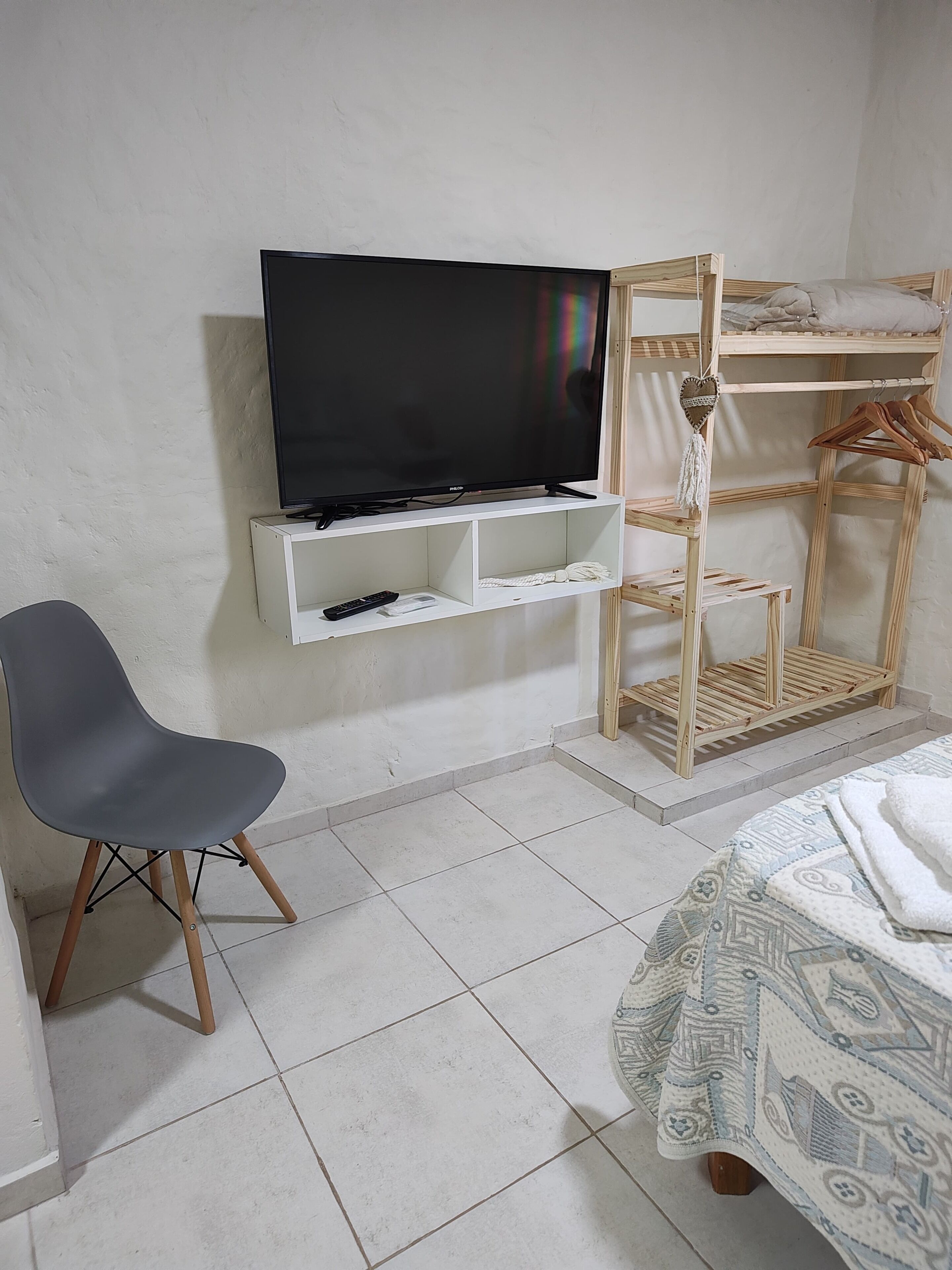A room with a television on a white shelf, a grey chair, a bunk bed, and a patterned bedspread.