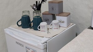 A kitchen with a white refrigerator, a coffee maker, and a microwave. There are also several containers labeled "TE," "CAFE," and "SUGAR."