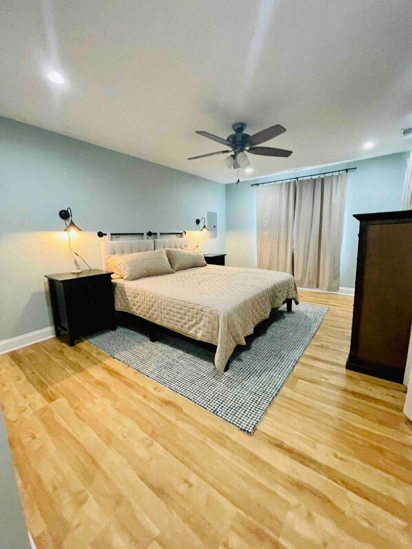 A bedroom with a bed, nightstands, a ceiling fan, and a window with curtains. - Cozy Riverfront Cabin: Parks,Kayaks& Island Charm (Momence)