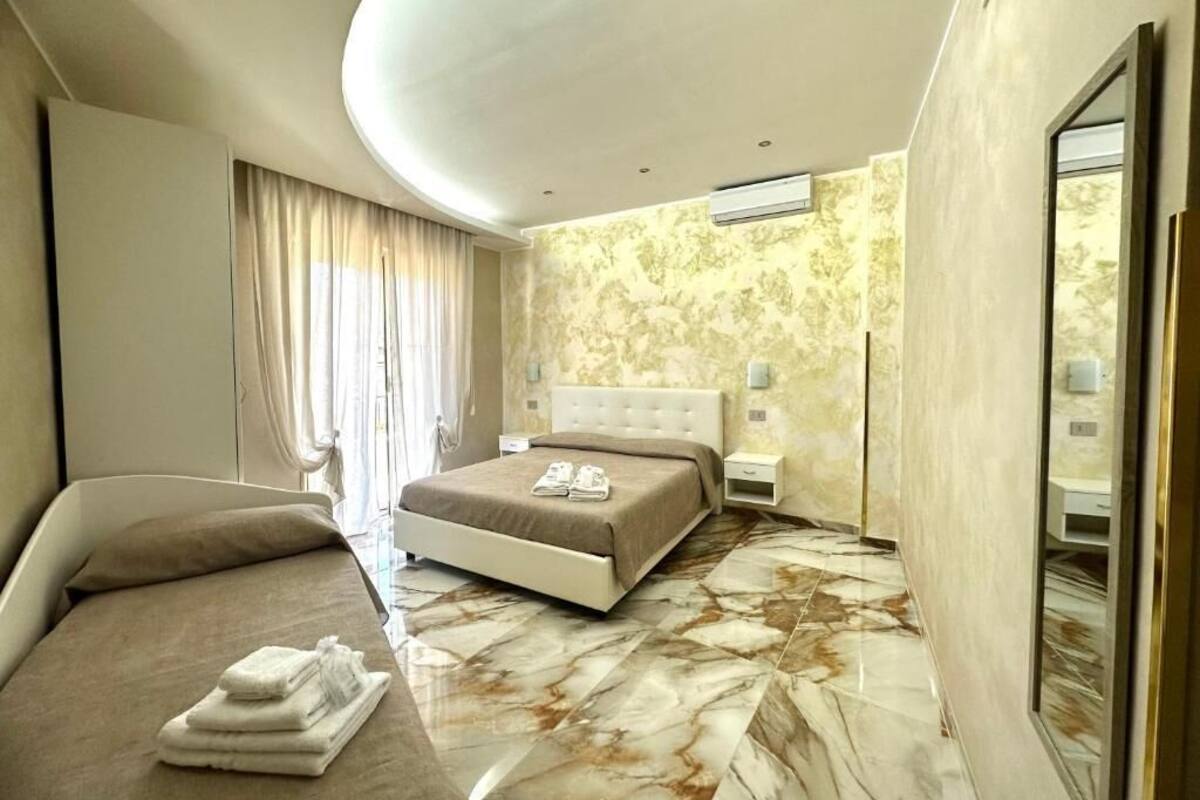 A modern hotel room with a large bed, a separate sofa, a vanity with a mirror, and a marble floor.