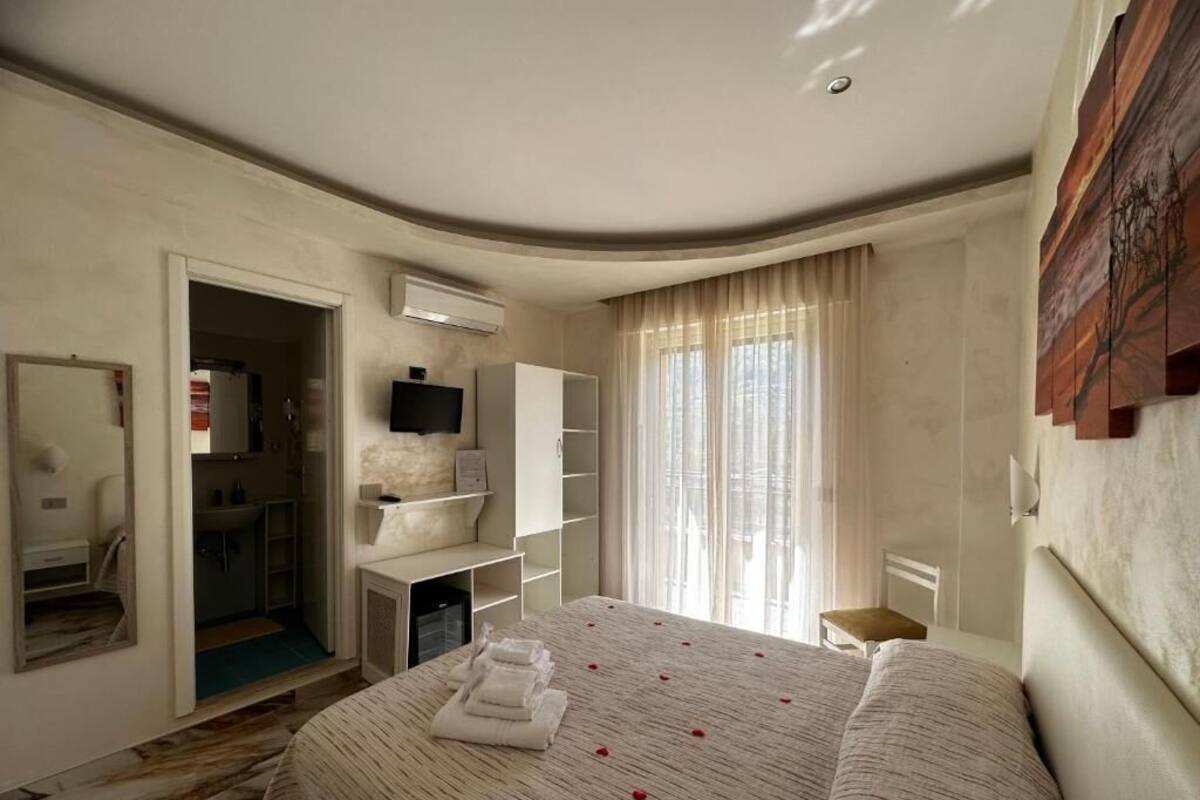 A hotel room with a large bed, a wardrobe, a desk with a chair, and a television.