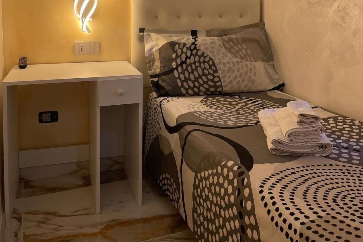 A bedroom with a bed, a desk, and a wall-mounted light fixture.