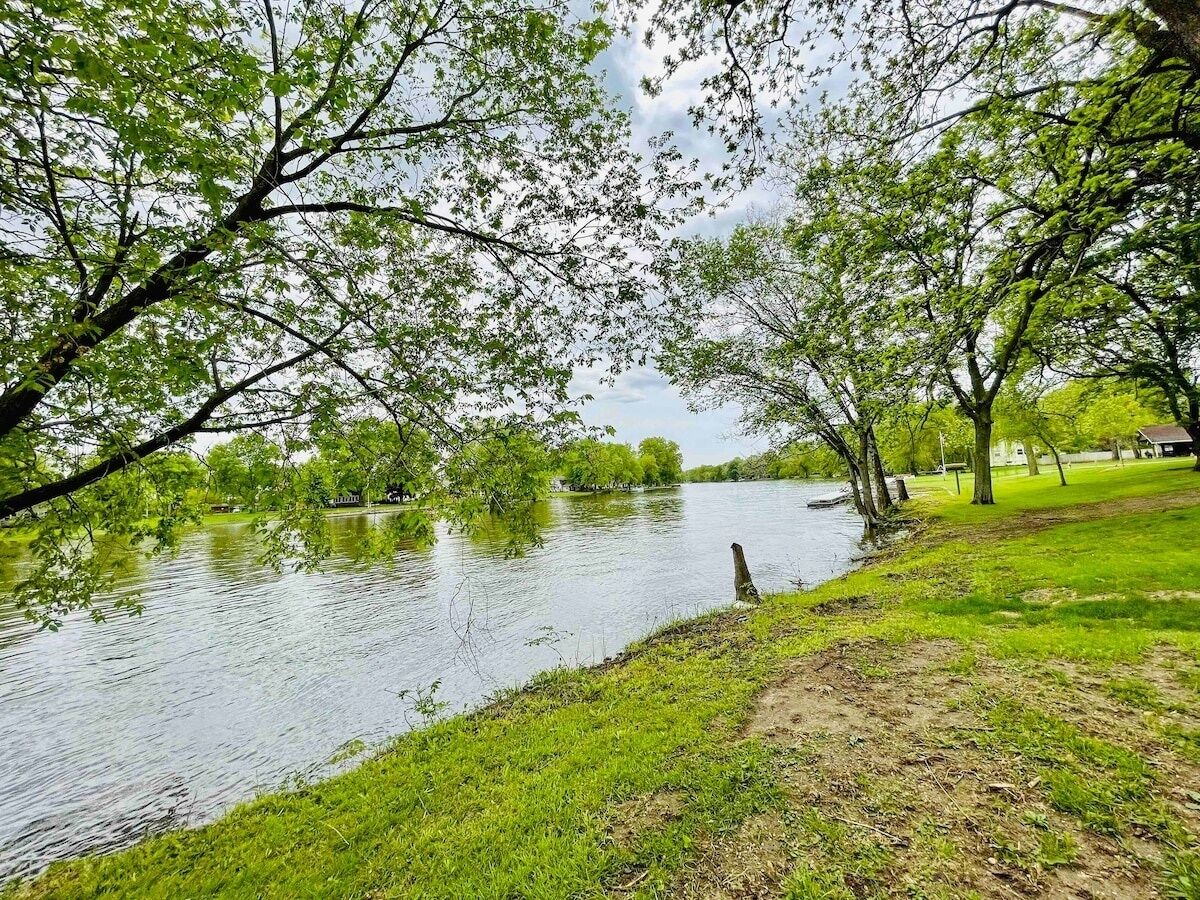 En flod med träd längs stränderna, ett grönområde och en klar himmel.