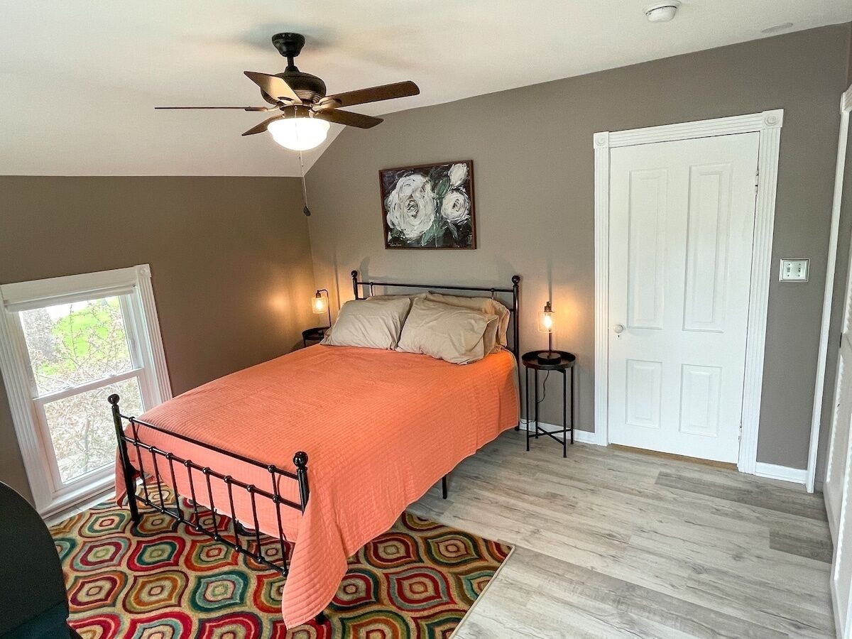 A bedroom with a bed, a ceiling fan, a door, and a window.