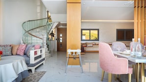 A spacious living area with a high ceiling, a glass staircase, a dining table with chairs, and a baby high chair. - Villa Perle mémorable séjour vous attendent (Tetouan)