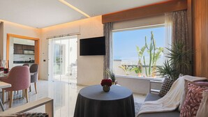 A modern hotel room with a dining area, a sofa, a TV, and a view of the city. - Villa Perle mémorable séjour vous attendent (Tetouan)