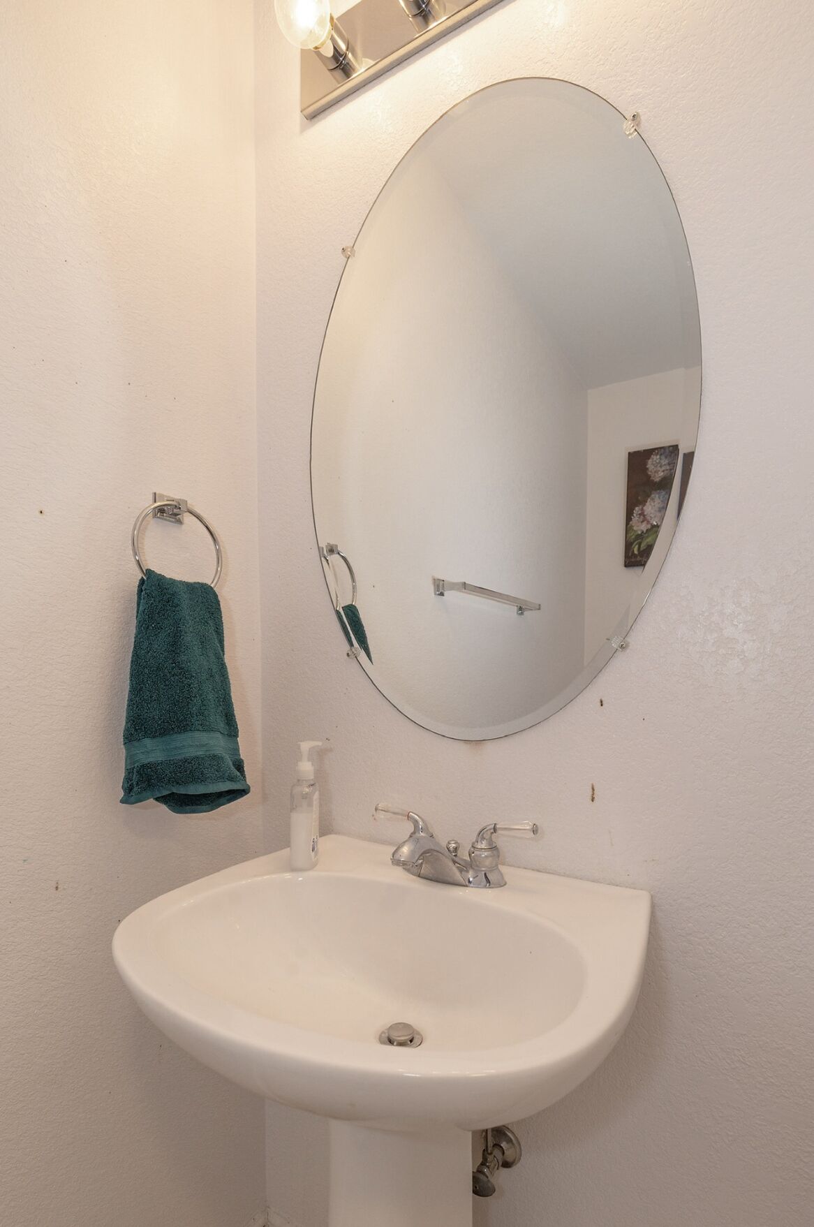 A bathroom with a white sink, a round mirror, and a green towel hanging on a metal ring.