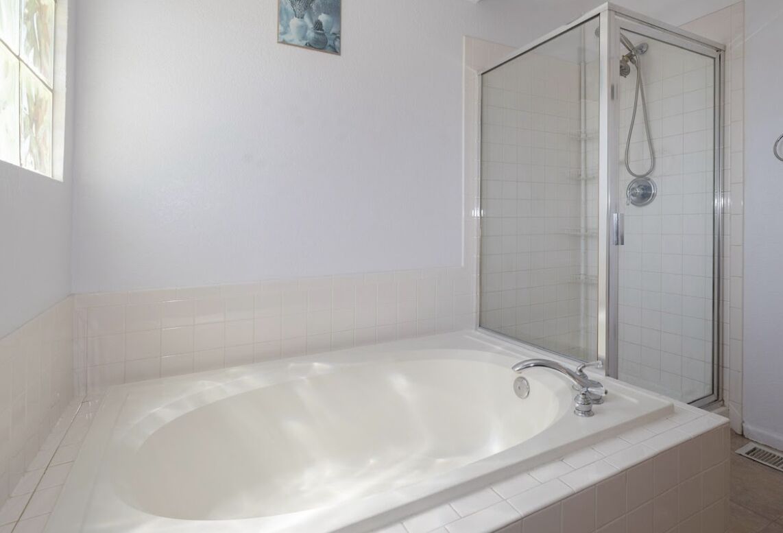 Un baño con una bañera grande, una ducha con mampara de vidrio y paredes de azulejos blancos.