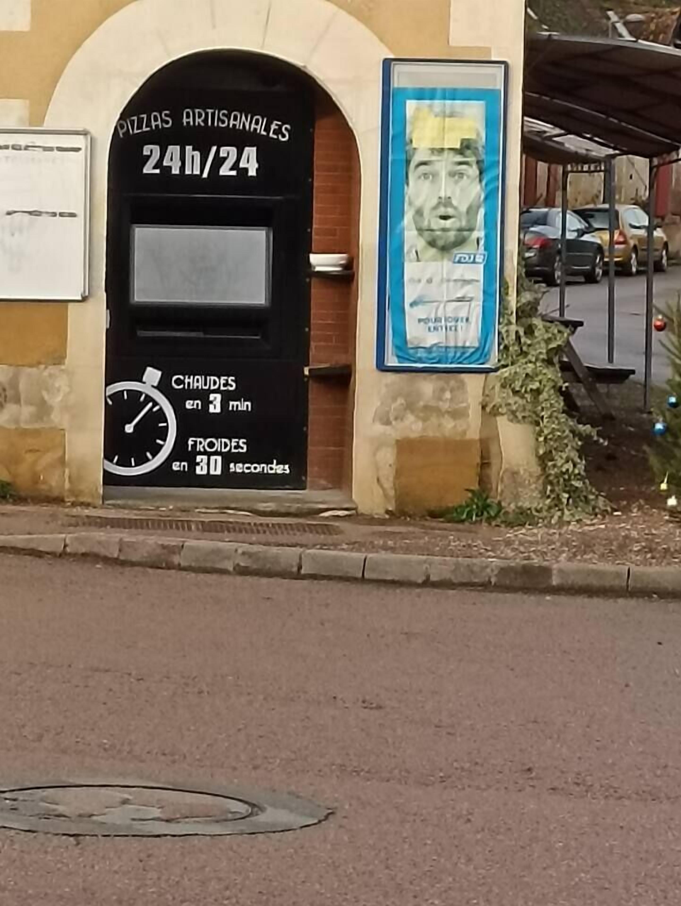 Un edificio con un letrero que dice "PIZZAS ARTISANALES 24h/24" y un reloj que muestra temperaturas.