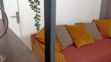 A room with a wooden table, a sofa with patterned cushions, a hanging plant, and a framed picture on the wall.