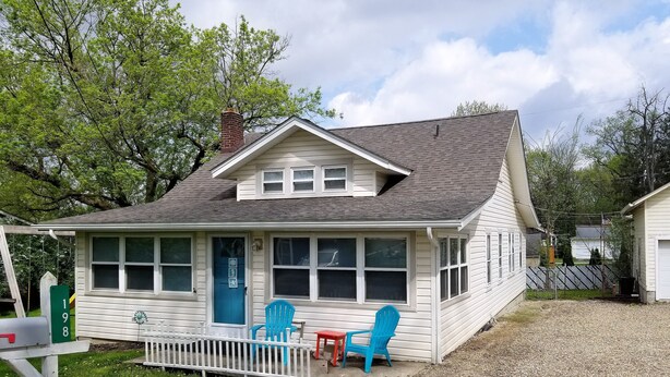 A single-story house with a front porch, two blue chairs, and a mailbox.