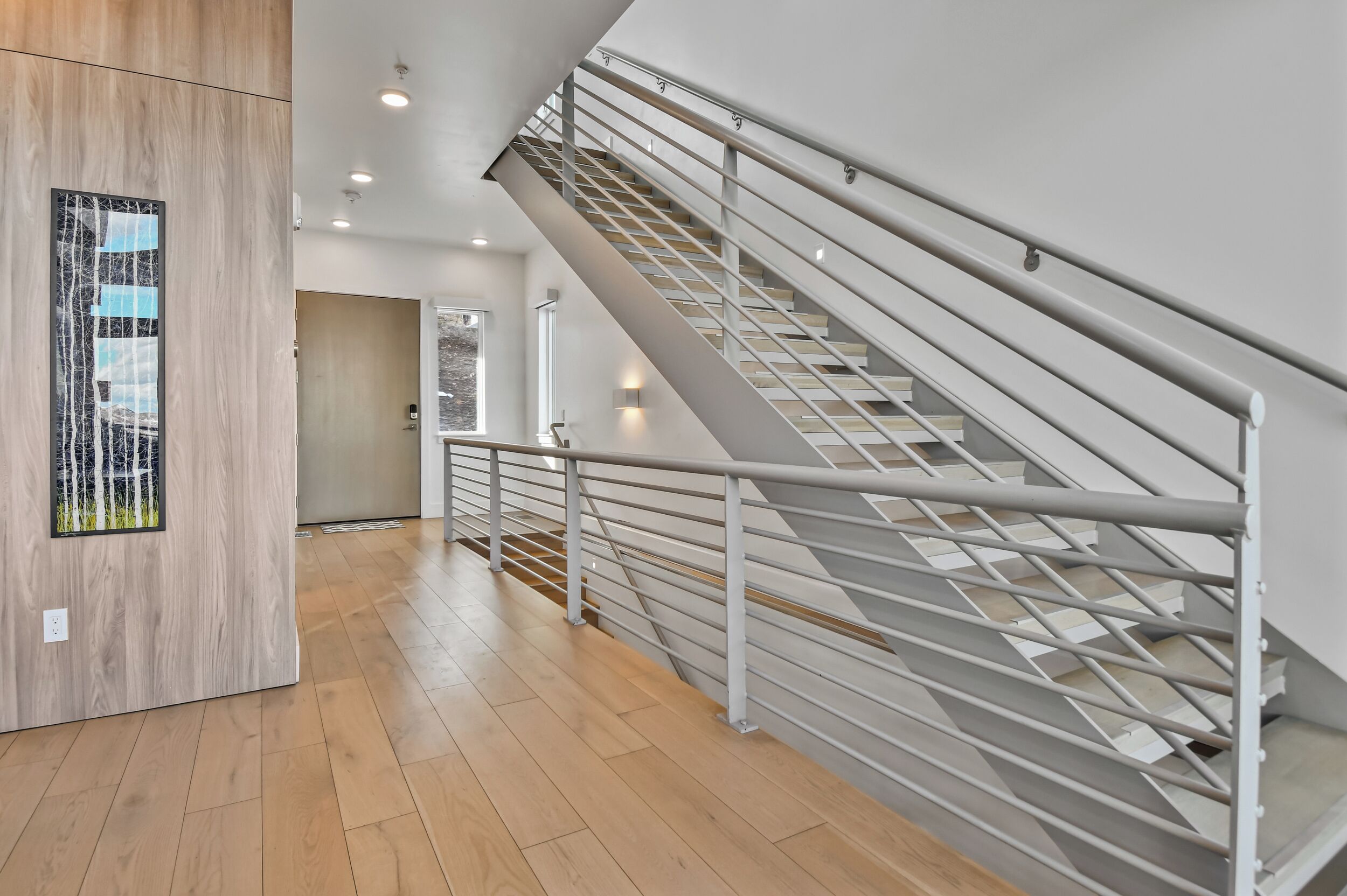 A modern interior with a wooden floor, a staircase with metal railings, and a wall-mounted light fixture.