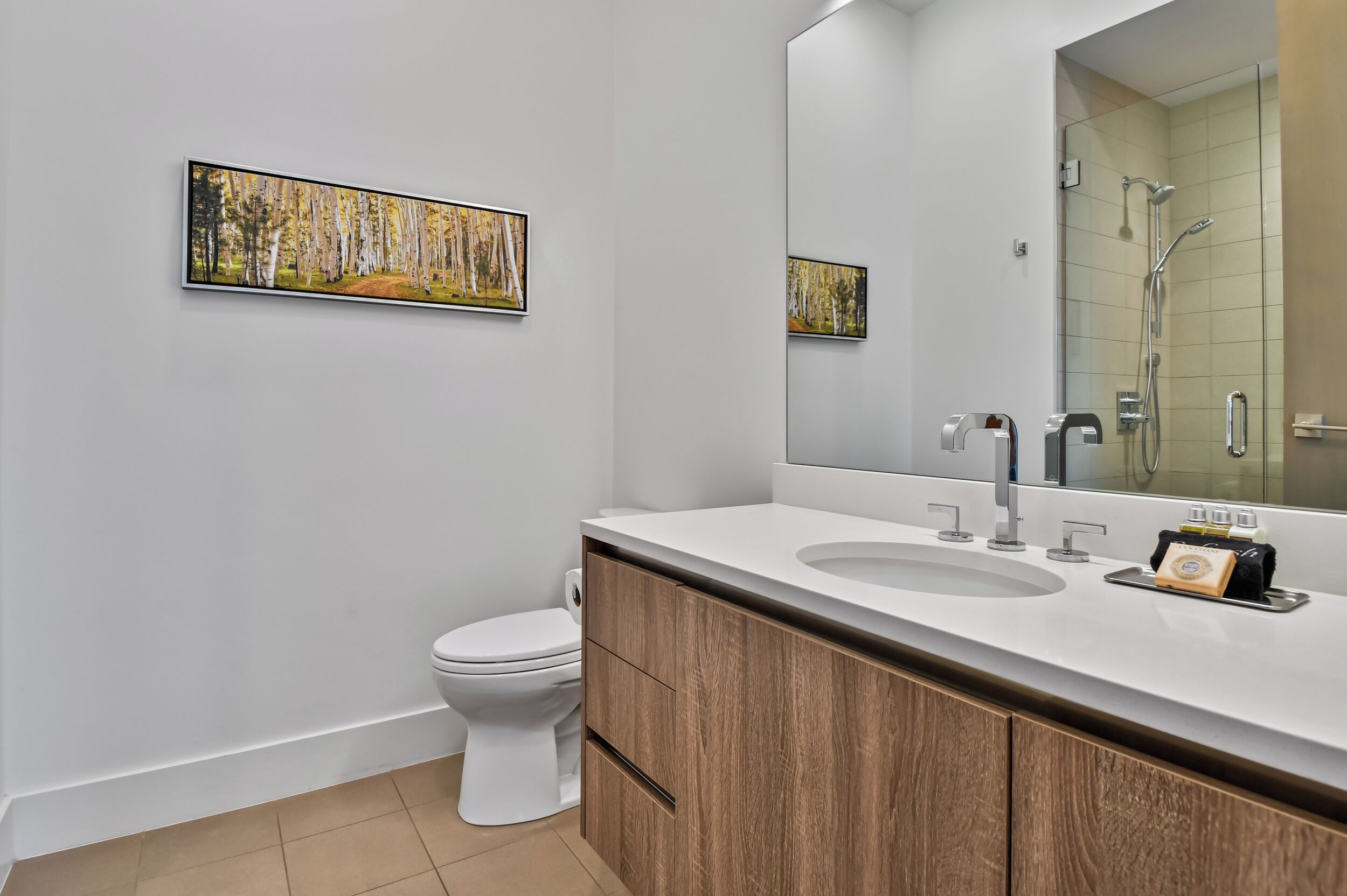 A modern bathroom with a white toilet, a large mirror, and a wooden vanity with a sink.
