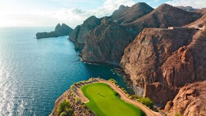 A golf course with a clear view of the surrounding rocky cliffs and the ocean.
