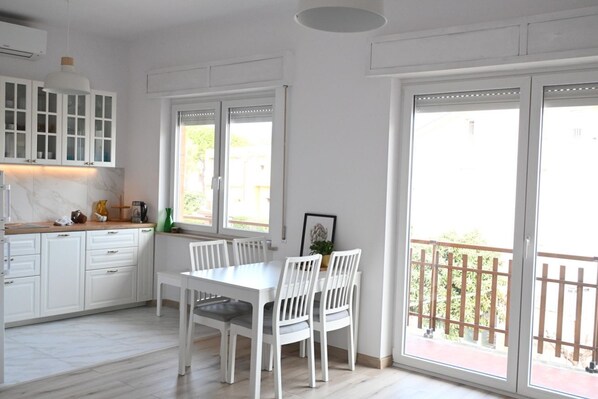 A modern kitchen with white cabinetry, a dining table with chairs, and large windows with a view of the outdoors.