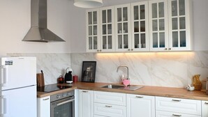 Une cuisine avec des armoires blanches, une hotte de cuisinière en acier inoxydable, un plan de travail en bois et un dosseret en marbre.