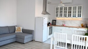 Une cuisine moderne avec des meubles blancs, un four encastré et un canapé gris.
